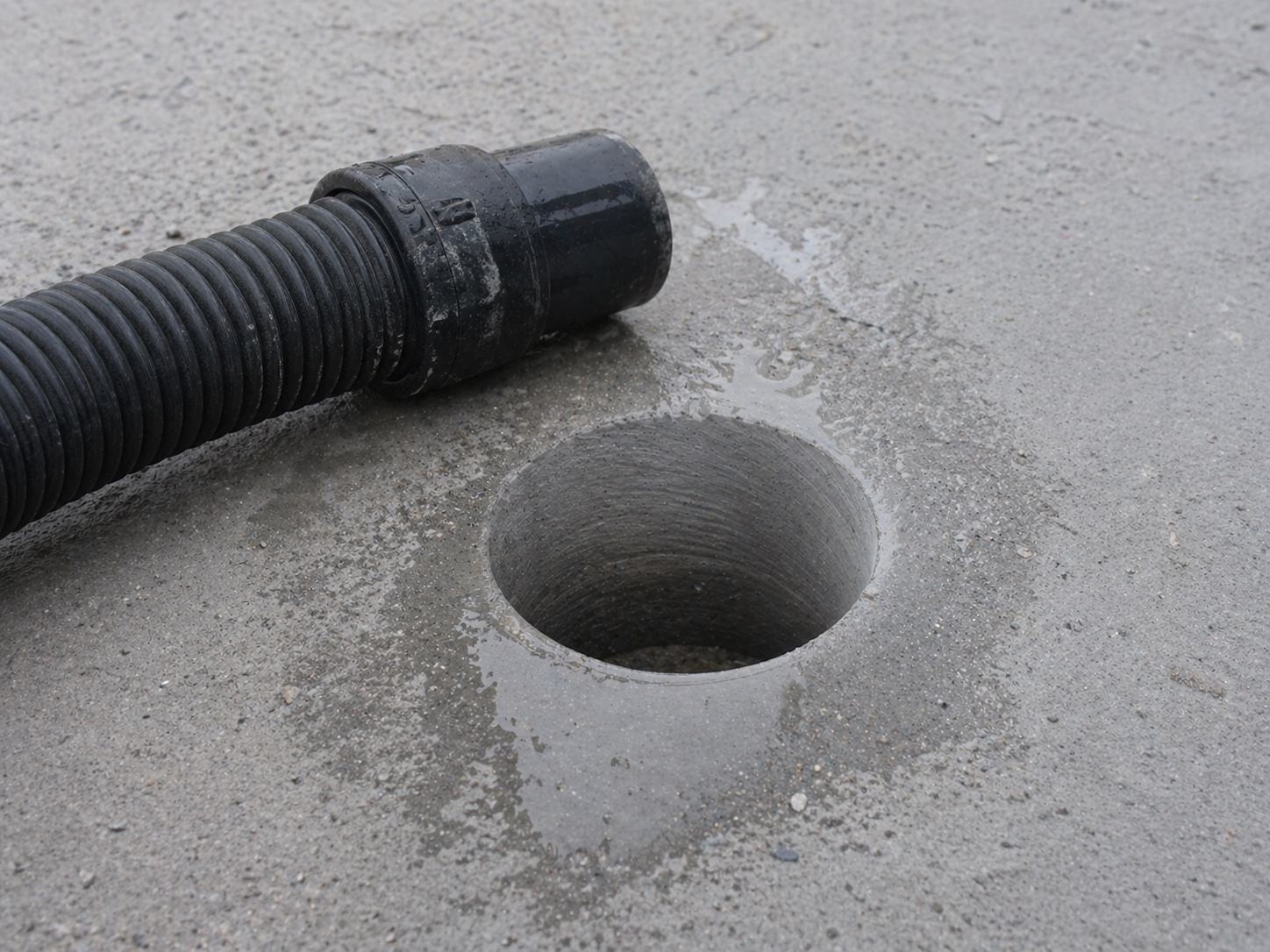 A clean drilled hole through a slab with a slurry-extraction hose alongside