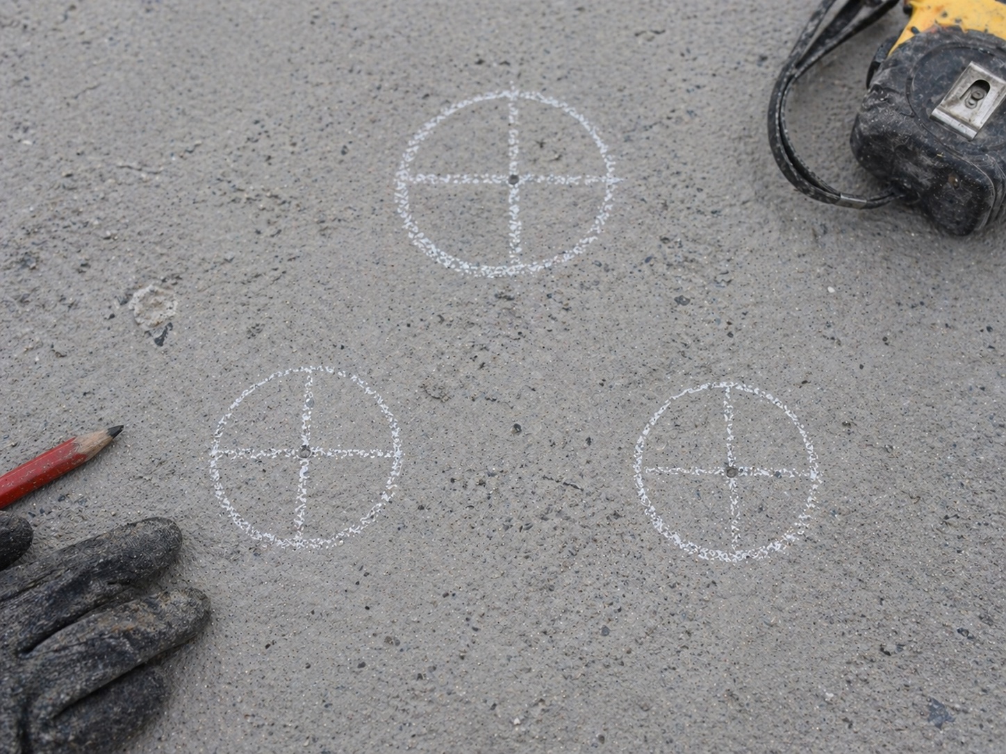 Crosshair set-out marks chalked on a concrete slab next to a tape measure and gloves